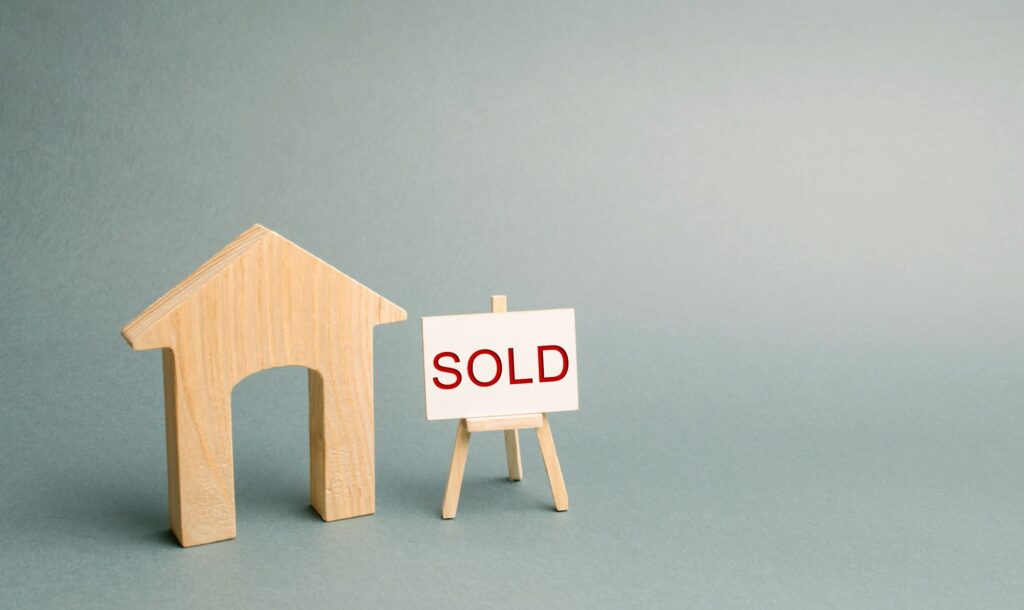 A miniature wooden house and a poster with the inscription Sold