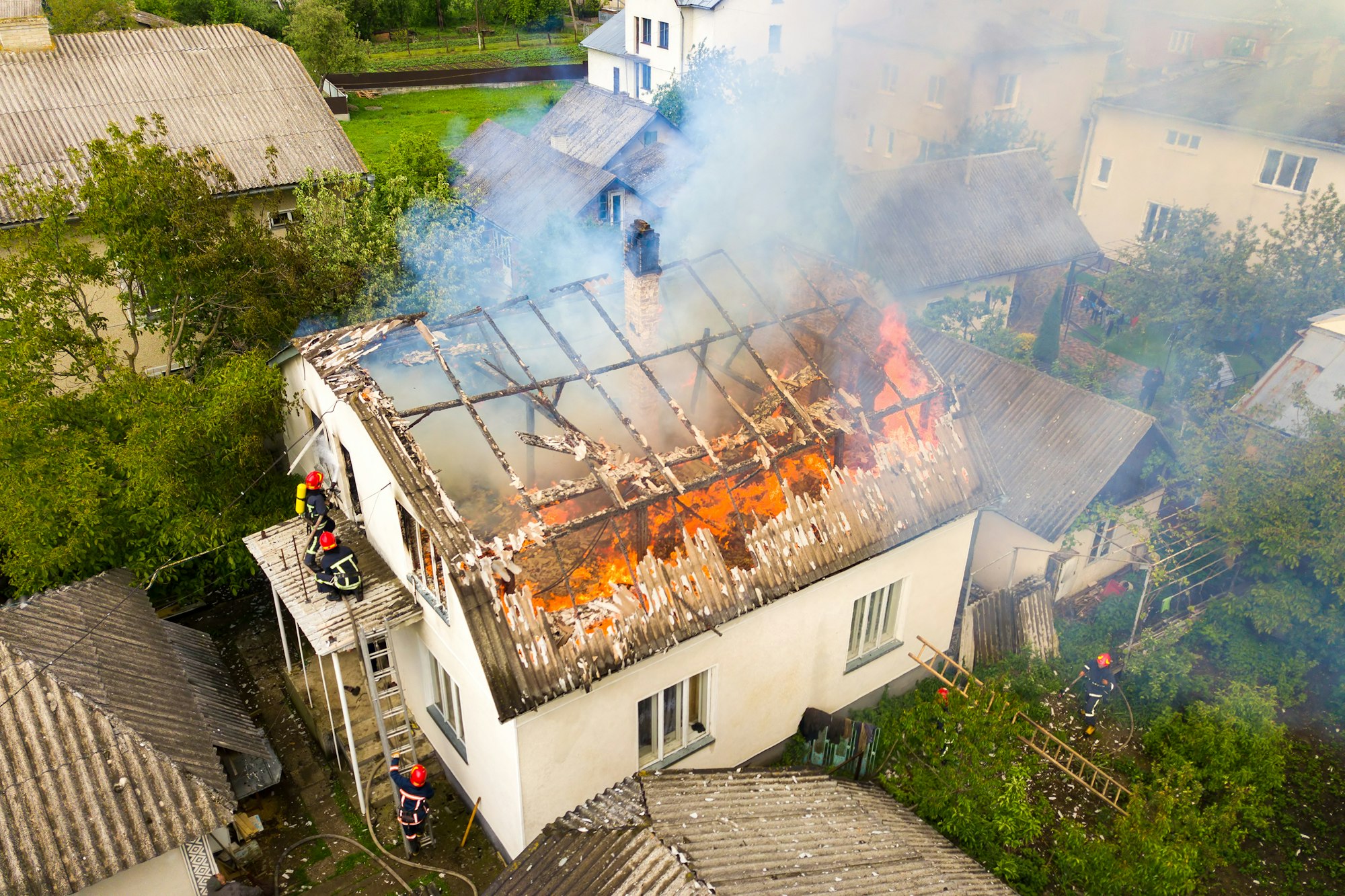 Aerial view of a house on fire with orange flames and white thick smoke