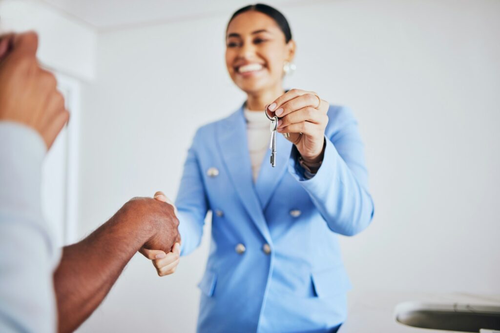 Moving in, house keys and female realtor shaking hands for congratulations with homeowner clients.